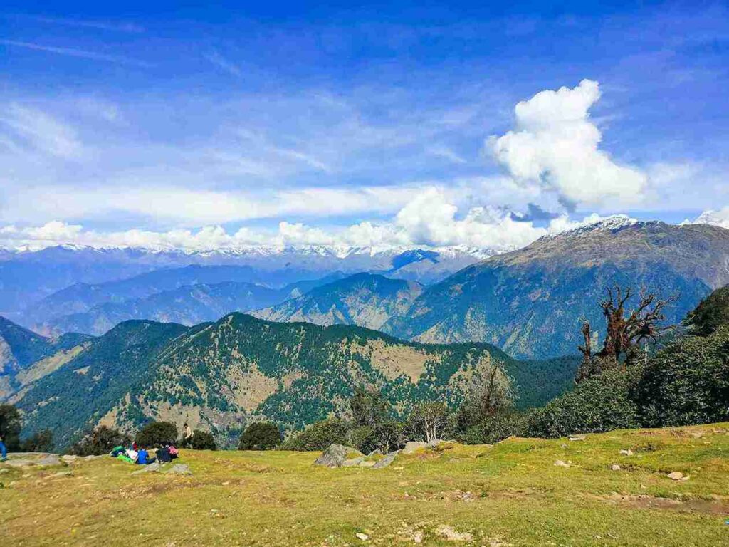 11 best places to visit in april  A scenic view of Kalpa village in Himachal Pradesh featuring traditional wooden houses with colorful roofs, a rainbow in the sky, and the snow-capped Kinnaur Kailash mountain range in the background.
