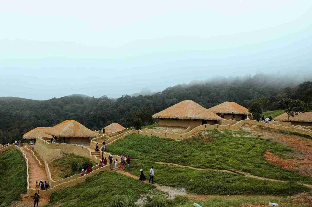 Traditional mud houses with thatched roofs in Wayanad Kerala surrounded by misty forest and walking trails, one of the 11 best places to visit in april in india