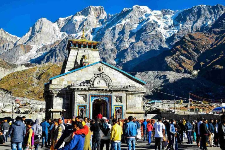 Devotees standing in front of the stone Kedarnath Temple with snow-capped Himalayan peaks behind it, a key part of our Kedarnath trip budget guide.