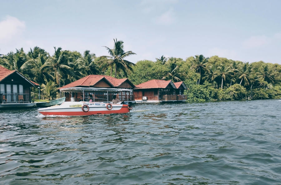 19 Best Places to Visit in December 2026: A scenic view of a motorboat cruising past floating cottages and palm trees in the backwaters of Poovar Island, Kerala.