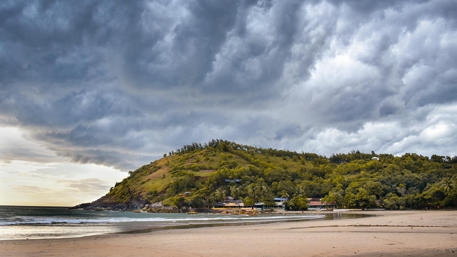 A beautiful sandy beach nestled against a lush green hill under dramatic stormy clouds, highlighting one of the 21 best places to visit in south.