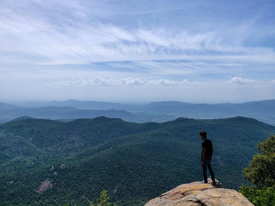 A traveler looking out over vast green valleys and hills from a rocky mountain peak viewpoint, featured in our list of the 21 best places to visit in south.