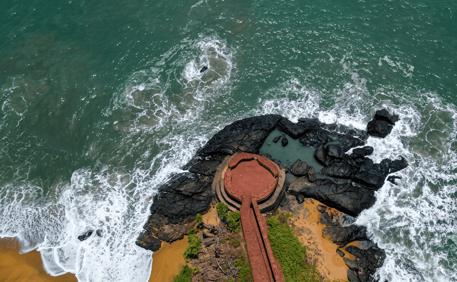 High-angle perspective of Bekal Fort's coastal stone pathway surrounded by foaming ocean water and dark rocks, highlighted among the best places to visit South India.