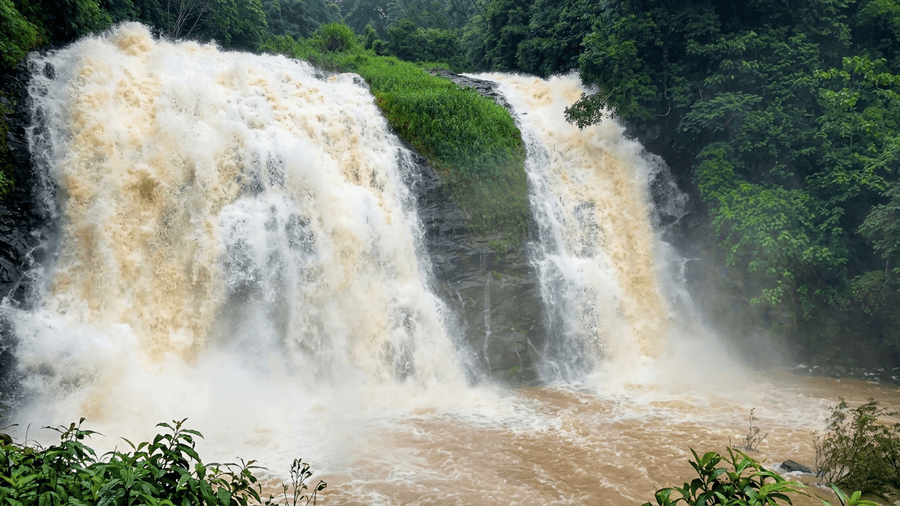 Heavy roaring waterfall cascading down rocky cliffs amidst dense greenery in Munnar, featured as one of the best places to visit in South India.