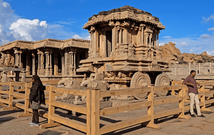 Tourists admiring the ancient Hampi Stone Chariot under a blue sky at the Vittala Temple in Karnataka, making it one of the top historic and architectural best places to visit in South India.