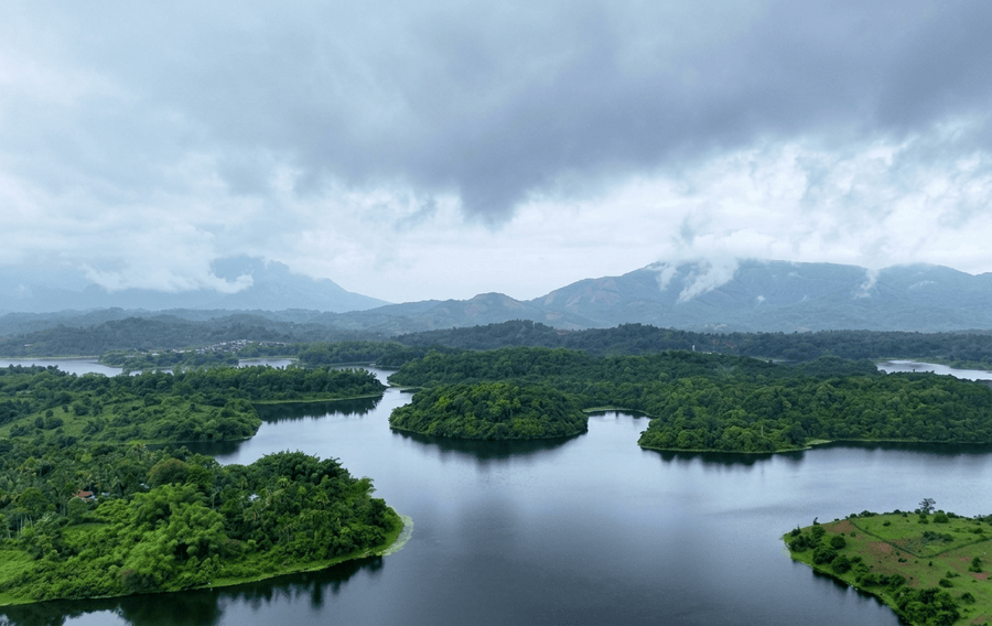 Mist-covered mountain peaks looming over expansive lake waters and forest islands in Wayanad, highlighted among the best places to visit South India.