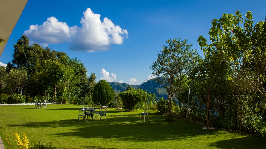 A lush green lawn with outdoor seating overlooking the Himalayan mountains in Binsar, Uttarakhand, one of the 19 best places to visit in December 2026.