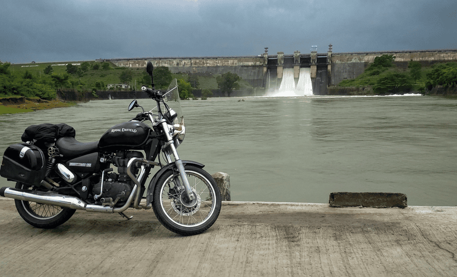 A black motorcycle parked near a river bank with the water cascading through the open gates of Harangi Dam, featured as one of the 23 best places to visit in Coorg in 2026.