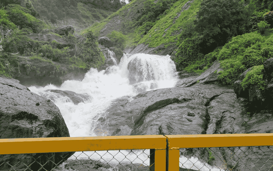 Gushing water cascading down rocks at Attukad Waterfalls seen from a bridge, a popular attraction in Munnar.