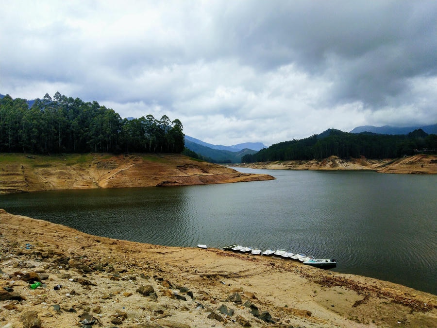 Speedboats lined up along the bank for boating at Mattupetty Dam lake surrounded by green hills in Munnar.
