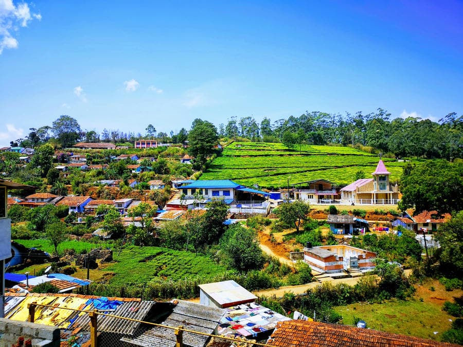 Scenic hill village in Kotagiri with terraced tea gardens and a local church under clear blue skies, highlighting hidden hill stations in South India 2026.