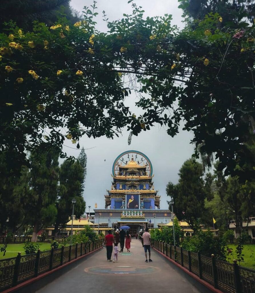 Visitors walking along the garden pathway toward Namdroling Monastery Golden Temple in Coorg, one of the best hill stations in South India with family in 2026.