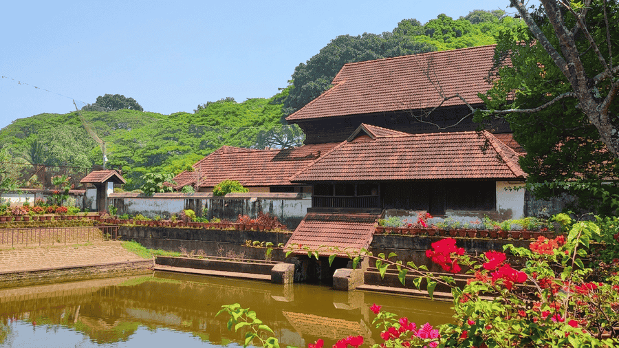 "Scenic view of the historic Krishnapuram Palace and pond in Alleppey, showing its traditional red-tiled roof and lush gardens with bougainvillea flowers, listed among the best places to visit in Alleppey, Kerala."