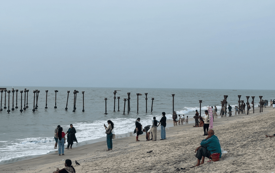 A wide shot of Alappuzha Beach featuring the iconic decaying iron pier pilings and structures extending into the Arabian Sea on a hazy day. This historic site is a major attraction and one of the best places to visit in Alleppey, Kerala, India.