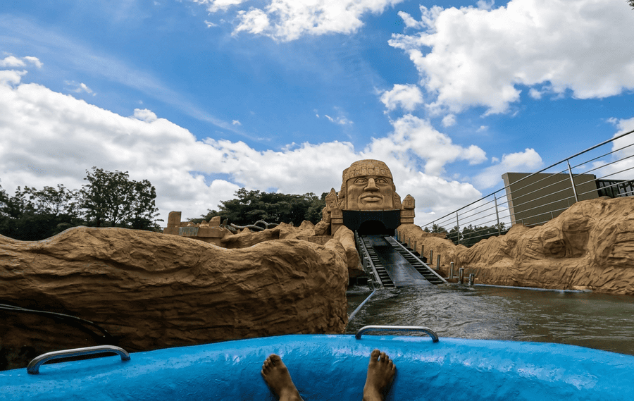 POV view from a blue inflatable raft floating toward a large stone face sculpture water slide at GRS Fantasy Park, featured among the 19 best places to visit in Mysore.