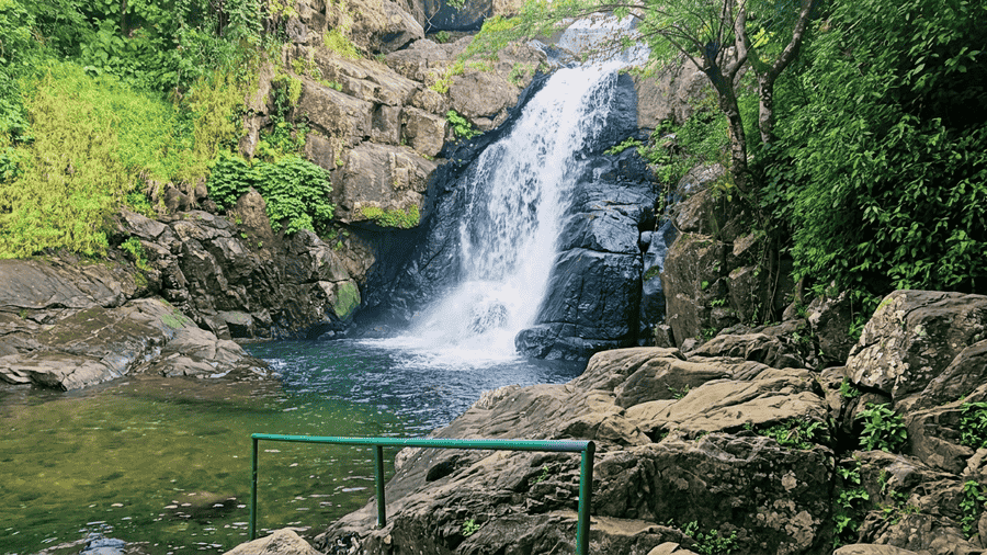 A stunning view of Meenmutty Waterfalls cascading down textured rocks into a green pool, recognized as one of the best places to visit in Wayanad for nature lovers and trekkers