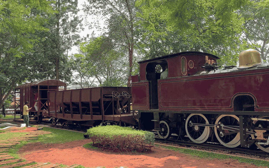 Visitors explore the vintage maroon steam locomotives and goods wagons displayed in the park setting of the Rail Museum Mysore, ranked among the 19 best places to visit in Mysore.