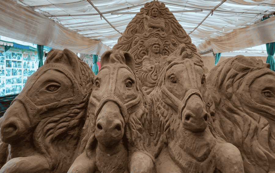A detailed sand sculpture depicting four large horses leading a chariot with divine figures, viewed at the Sand Sculpture Museum, one of the 19 best places to visit in Mysore.