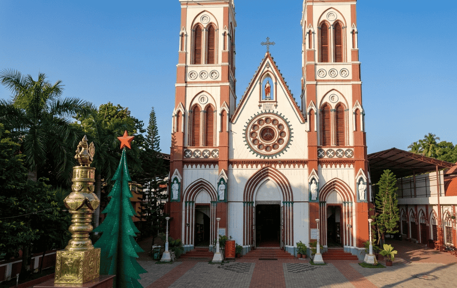 A full front view of the Basilica of the Sacred Heart of Jesus in Pondicherry featuring its iconic red and white Gothic Revival architecture, twin spires, and a large rose window. It is celebrated as one of the best places to visit Pondicherry for its historical and architectural beauty.