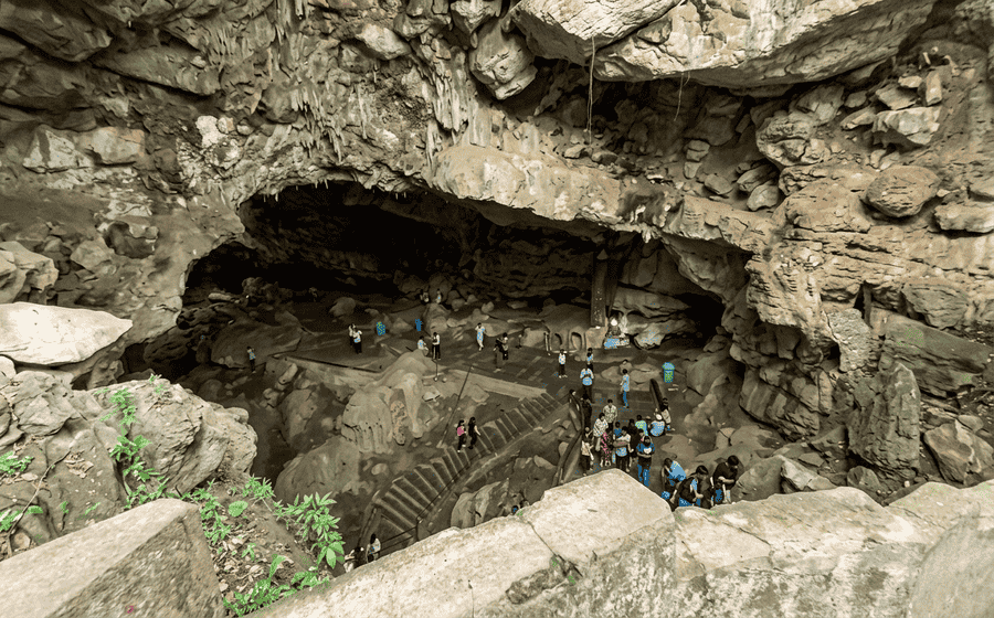 A high-quality panoramic view looking down into the massive limestone Borra Caves, featuring cascading stairs and tourists, listed as one of the best places to visit in Araku Valley.
