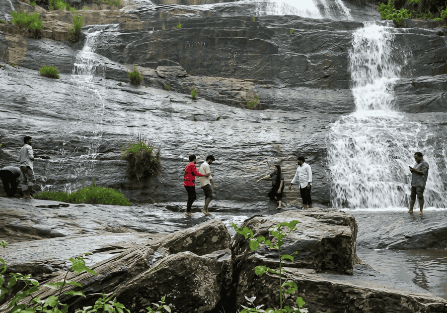 A group of people standing and interacting on the lower tiers of the scenic Tadimada Waterfall, a must-see destination featured among the best places to visit Araku Valley.