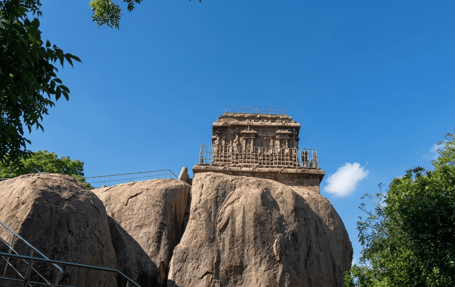 An outdoor view of the historic rock-cut Mahishasuramardini Cave nestled on a rocky hill, featured as one of the best places to visit Mahabalipuram.