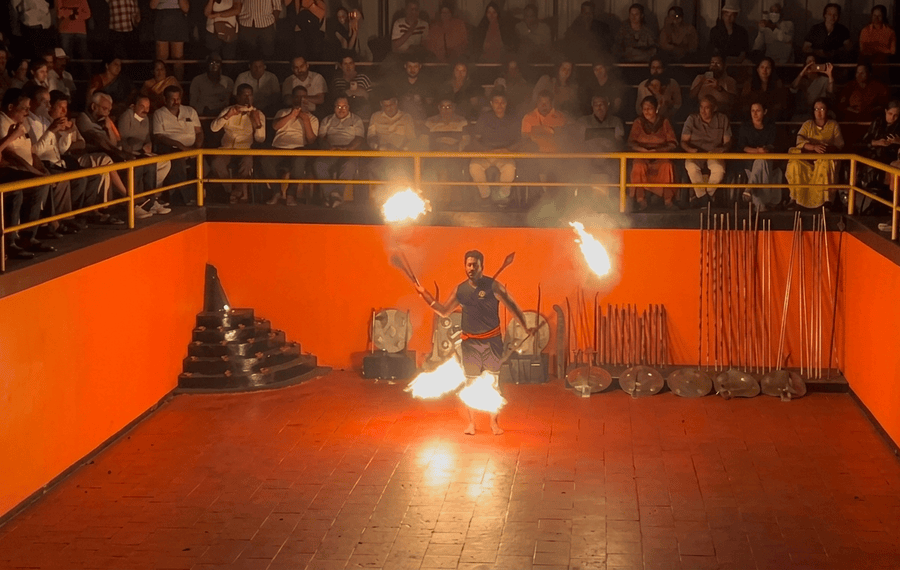 A martial arts performer spinning flaming weapons in front of a seated audience at Kadathanadan Kalari Centre, highlighted among the best places to visit Thekkady.