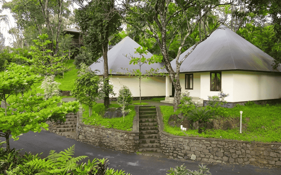 Pyramid-roofed eco-resort cottages nestled among lush green trees and manicured lawns in Kumily, featured as one of the best places to visit in Thekkady.