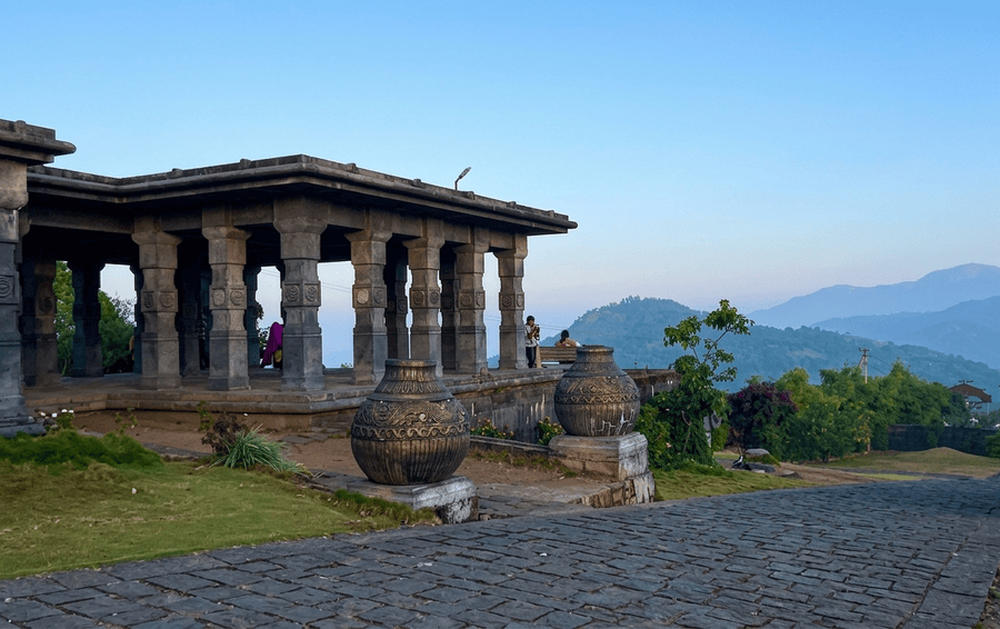 Traditional stone mantapa pillar structure and ornamental pots on a cobblestone hill path at Panchalimedu viewpoint, featured as one of the best places to visit in Thekkady.