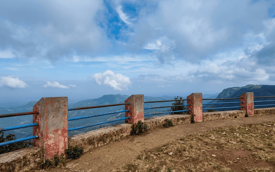 Weathered concrete supports and blue metal railing framing a stunning view of the Yercaud hill range from Gent's Seat. A must-see destination among the best places to visit in Yercaud.
