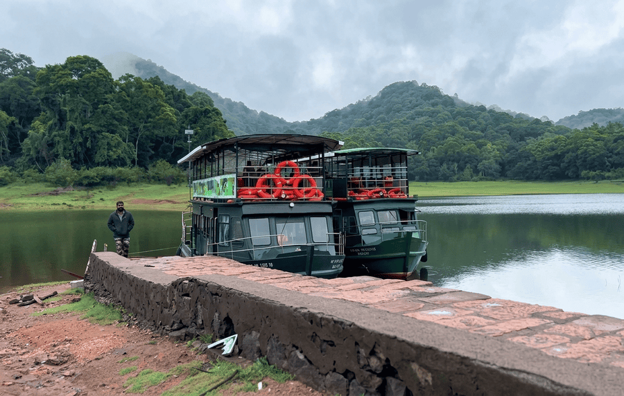 Two safari boats docked at the stone embankment of Periyar Lake, surrounded by lush green hills, featured as one of the best places to visit in Thekkady.