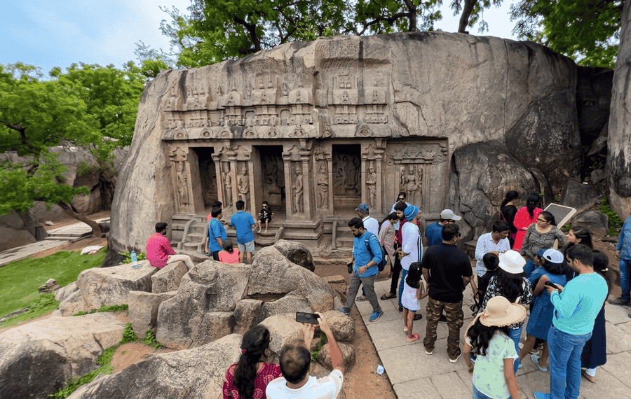 Visitors and tourists gathered around the massive granite boulder containing the Trimurti Cave, a famous historic monument among the best places to visit in Mahabalipuram.