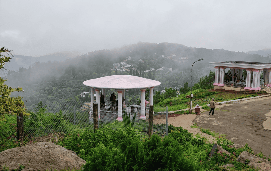 A scenic misty view of the pavilions at Lady's Seat viewpoint overlooking the lush green hills, one of the best places to visit in Yercaud.